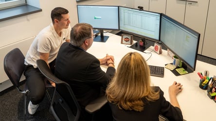 Ausbildungsleiter sitzt mit 2 Studierenden im Büro und arbeitet.