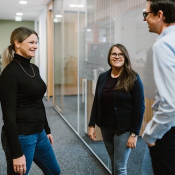 Gruppe von 3 Personen steht im Gang vor Glaswand.